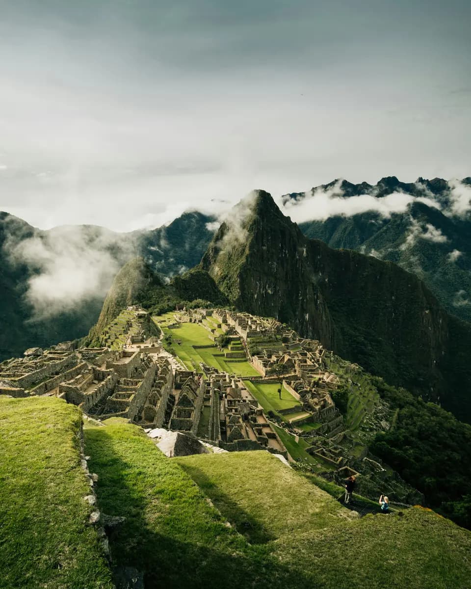 Machu Picchu ruins surrounded by steep green mountains and drifting cloud.
