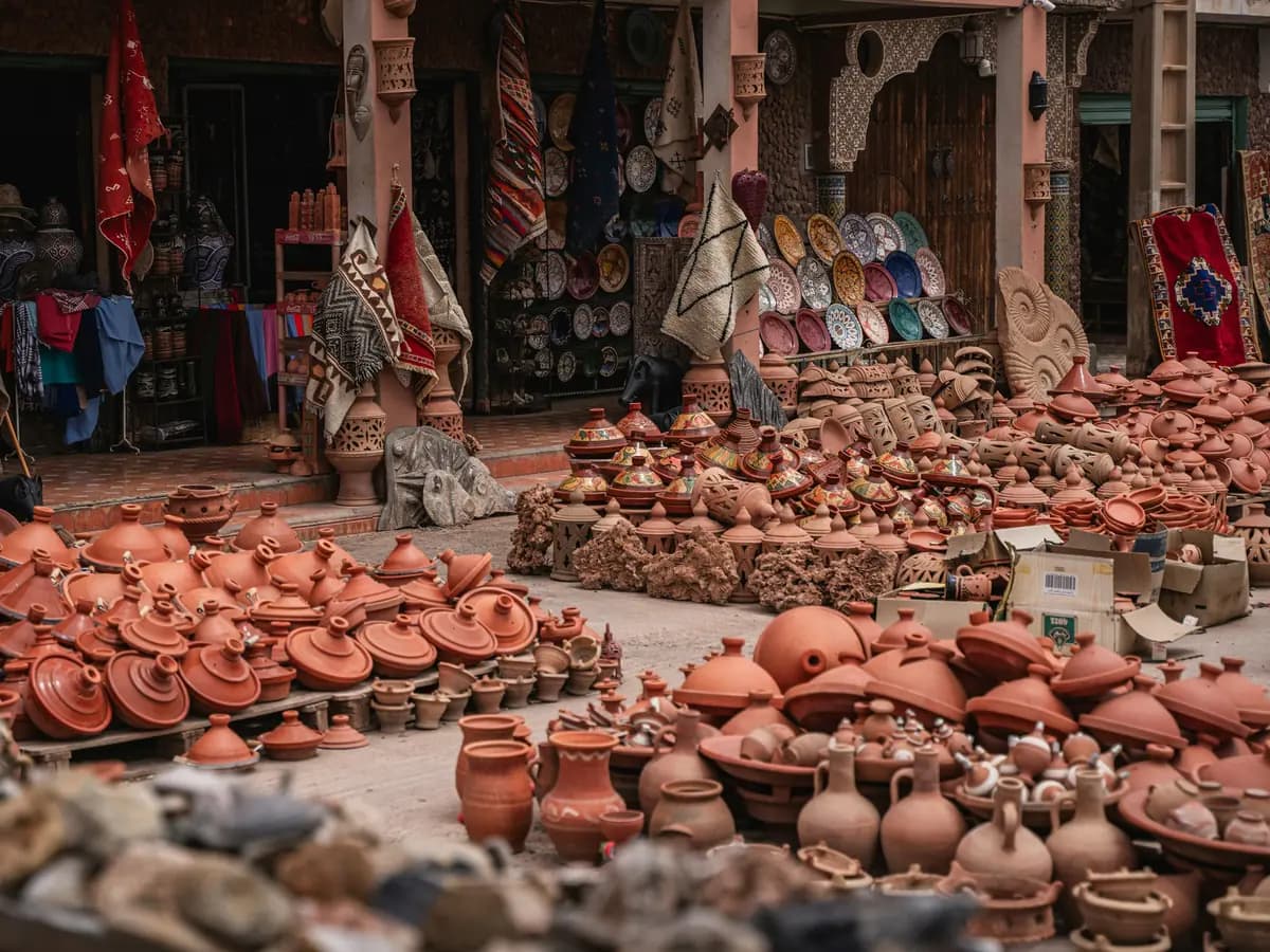 Outdoor craft market filled with terracotta pots, patterned ceramics, and woven rugs.