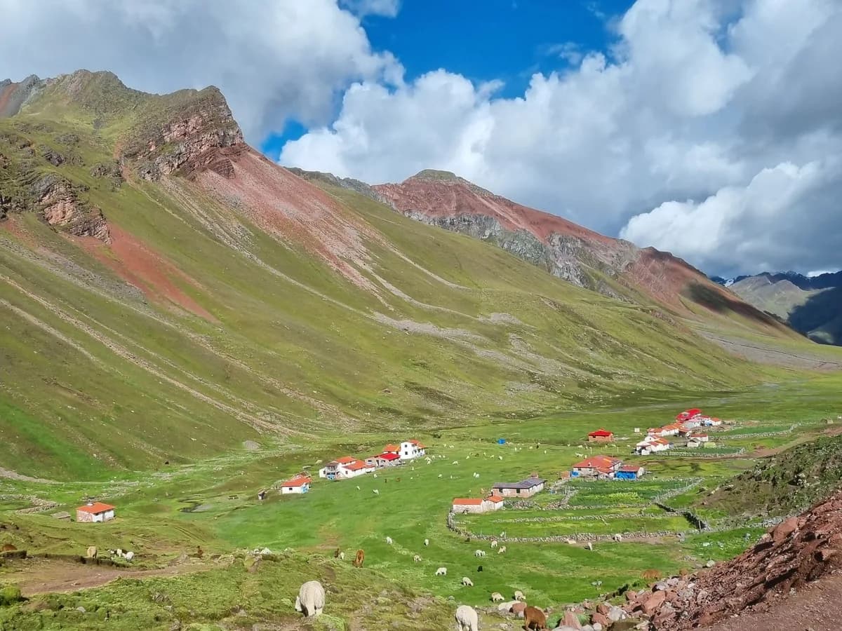 Green highland valley and village beneath red Andean ridges in Cusco, Peru.